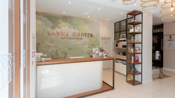 A reception desk with a sign reading "LANNA BONITA Boutique Hotel" and a modern interior with a wooden reception desk, a glass partition, and a shelving unit with various items. - Lanna Bonita Boutique Hotel (Chiang Mai)