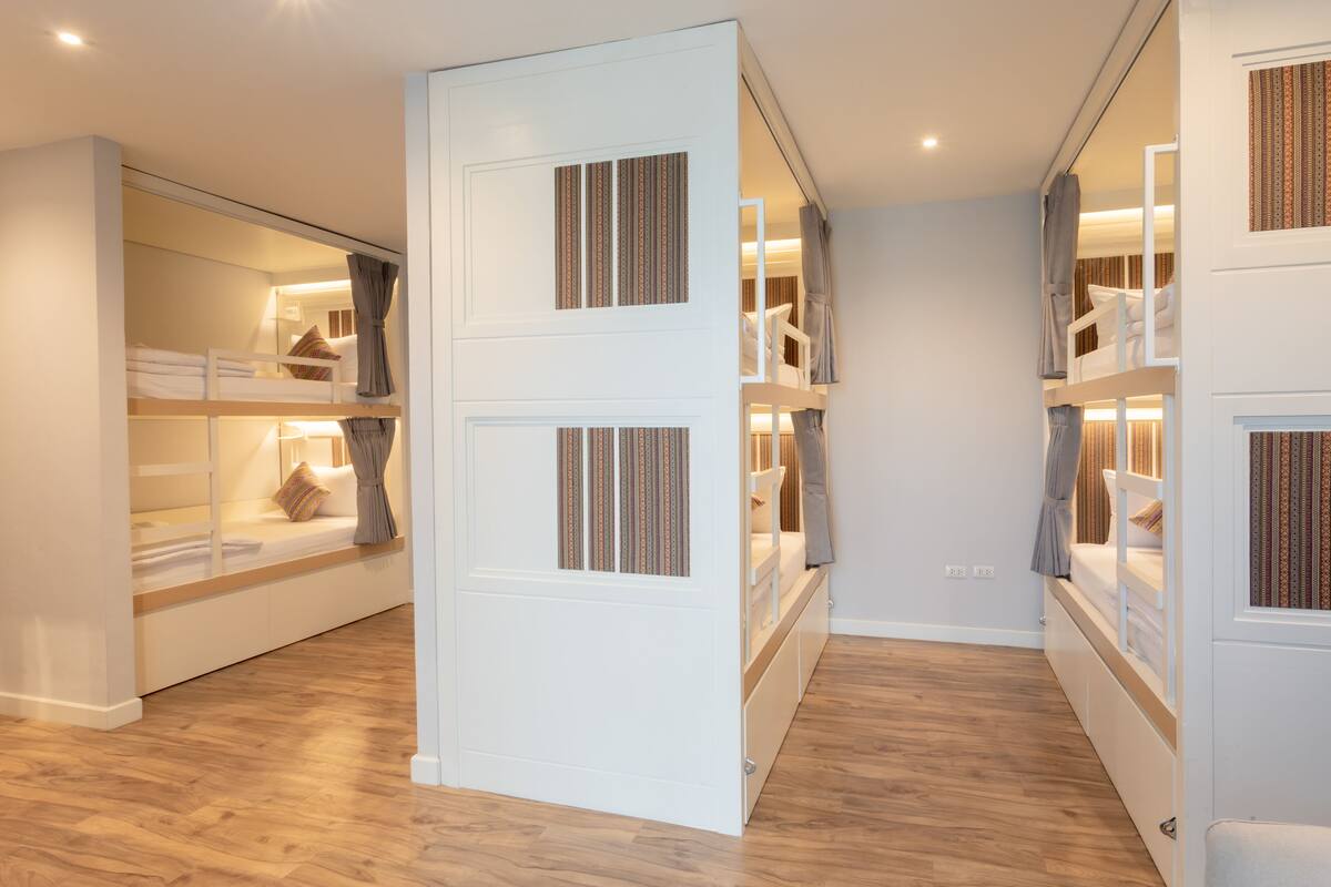 A hotel room with bunk beds, a wooden floor, and a white wardrobe.