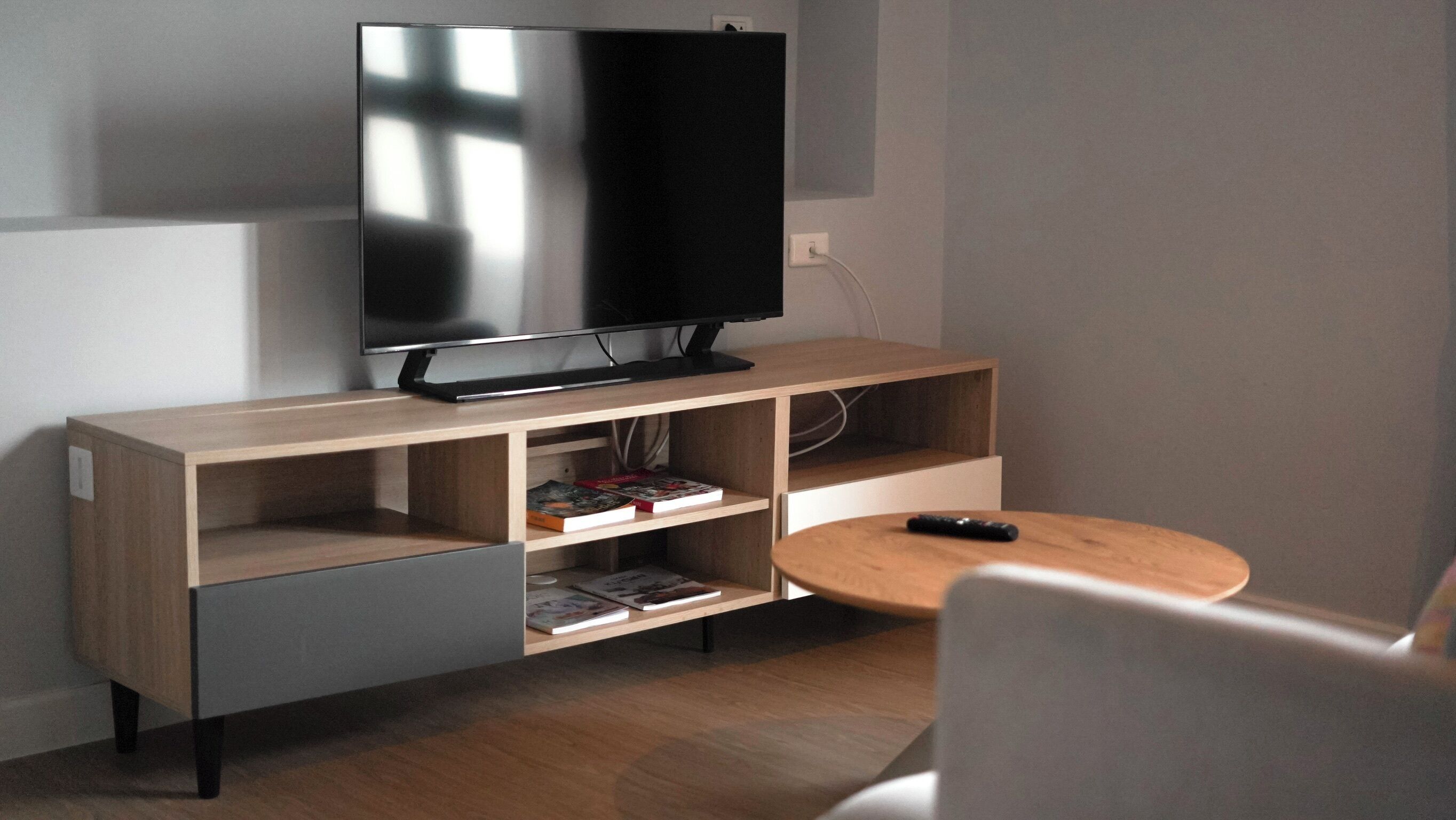 A modern living room with a flat-screen TV on a wooden stand, a small round table, and a grey sofa.