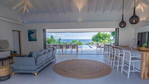 A spacious living room with a large sofa, a round rug, and a view of the ocean through an open door. - Villa prestige Sea view & beach access path (Saint-François)