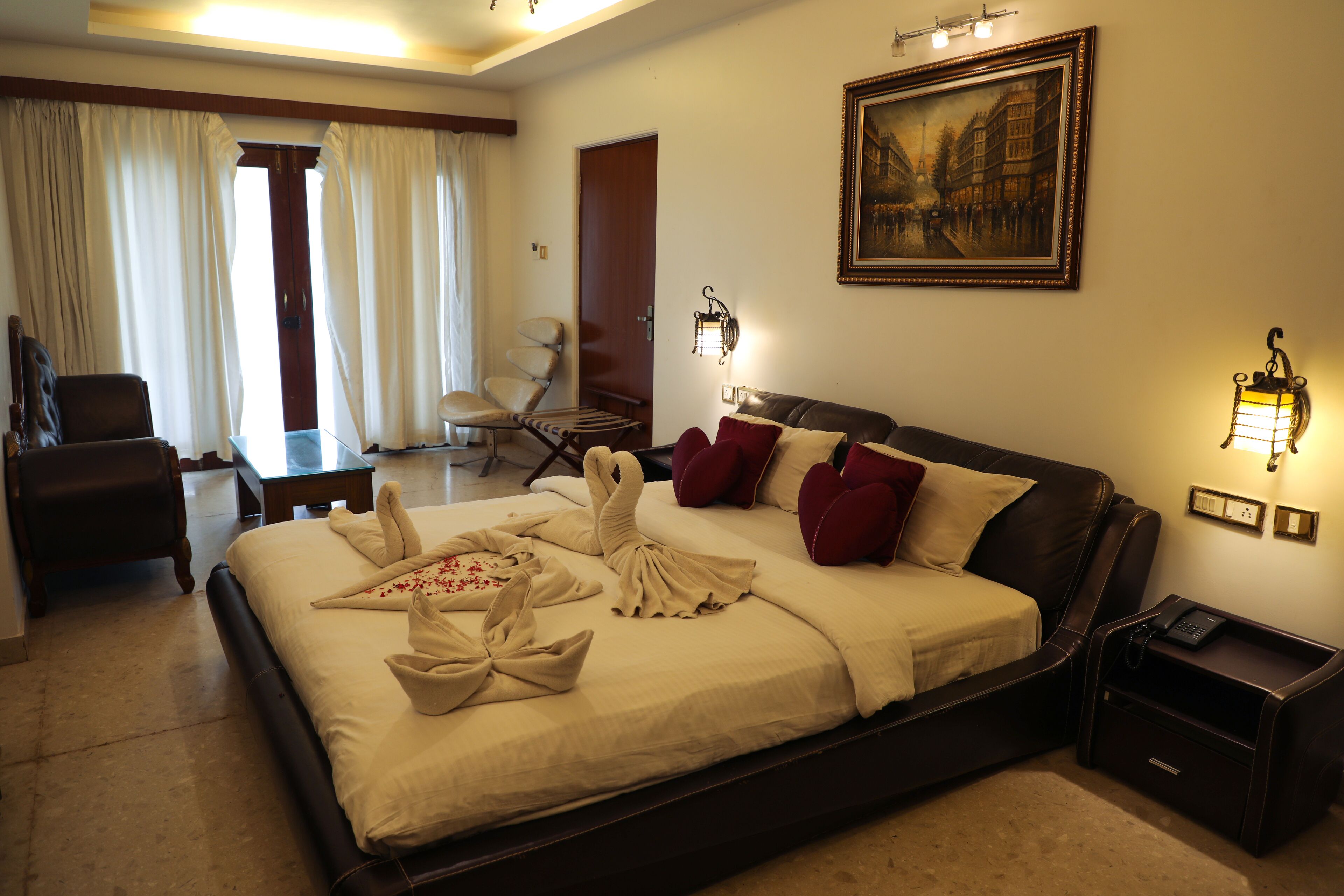 A hotel room with a large bed, a desk, a chair, and a painting on the wall.
