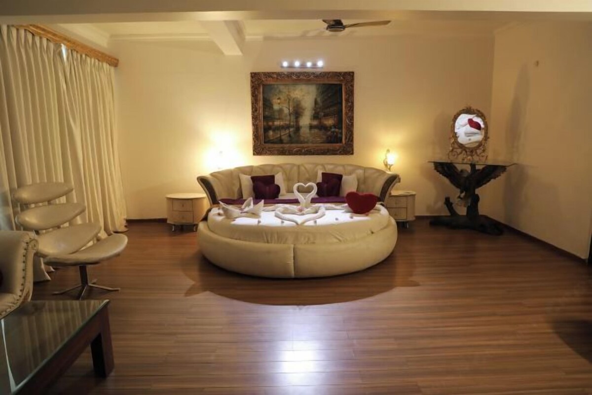 A living room with a round sofa, two armchairs, a coffee table, a painting on the wall, and a decorative mirror.