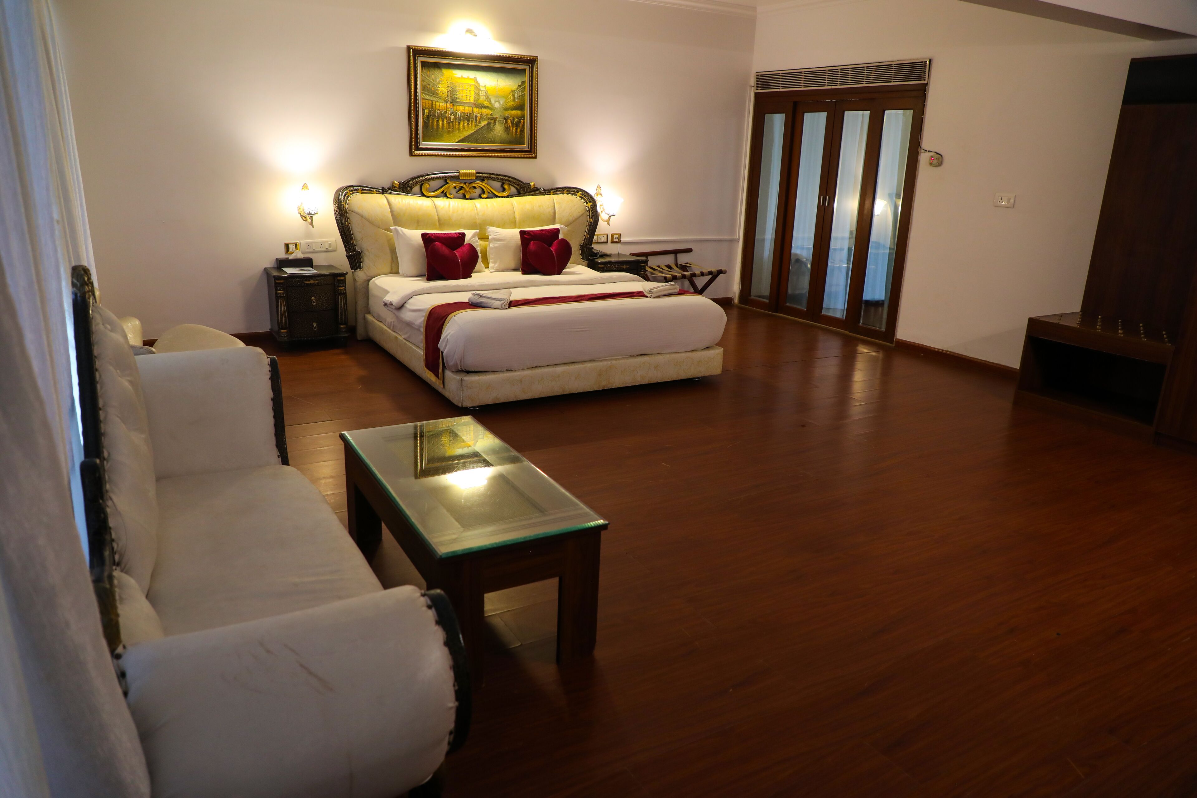 A hotel room with a bed, a sofa, a small table, and a painting on the wall.