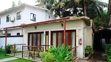 A two-story building with a covered entrance, a fire extinguisher, and a small garden area with potted plants.