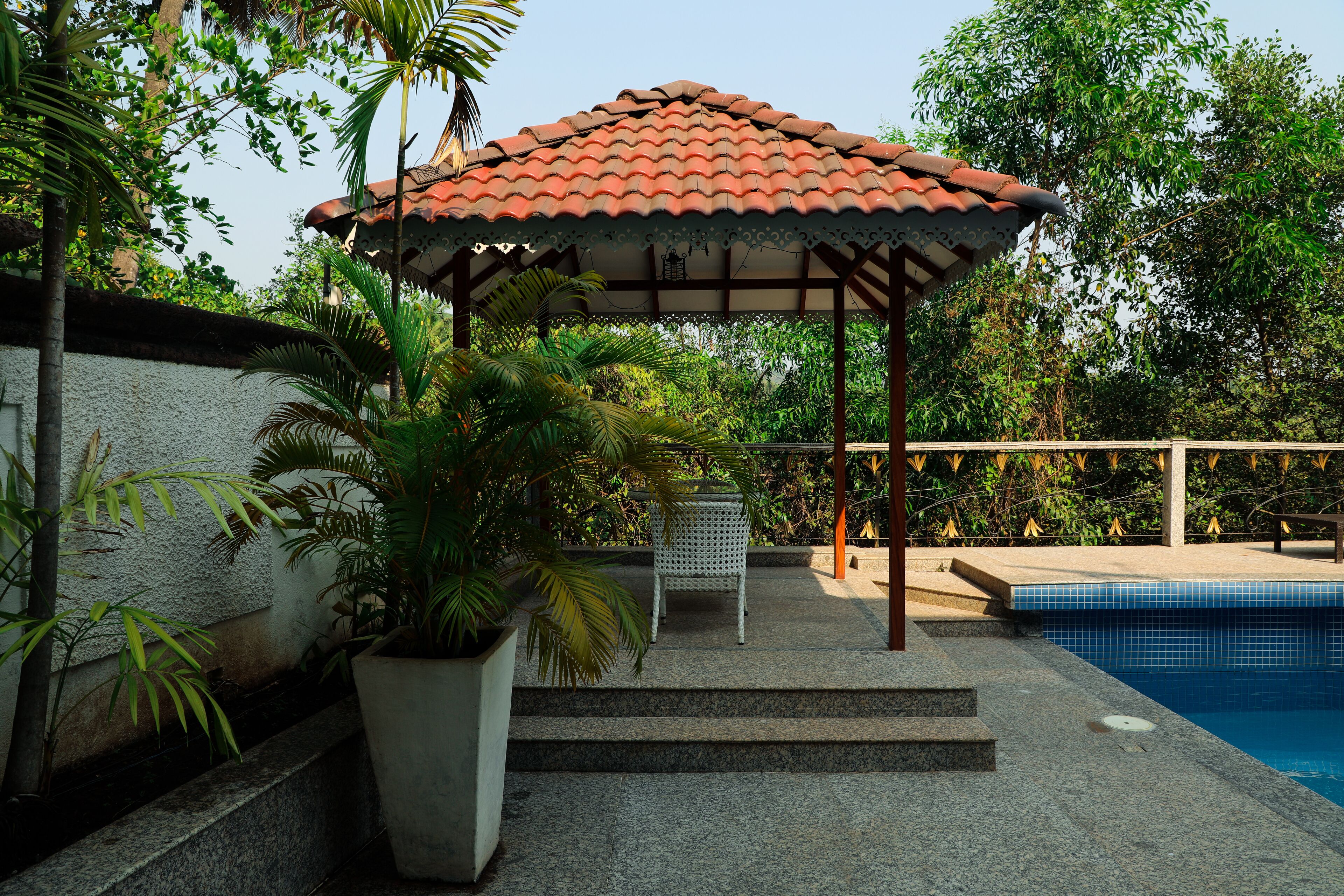 A covered outdoor area with a pool, steps leading to a gazebo, and potted plants.