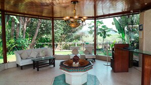 A spacious indoor area with a wooden ceiling, a central decorative fountain, a white sofa, and a glass table. - White Pearl Suites by Rosetum (Calangute)