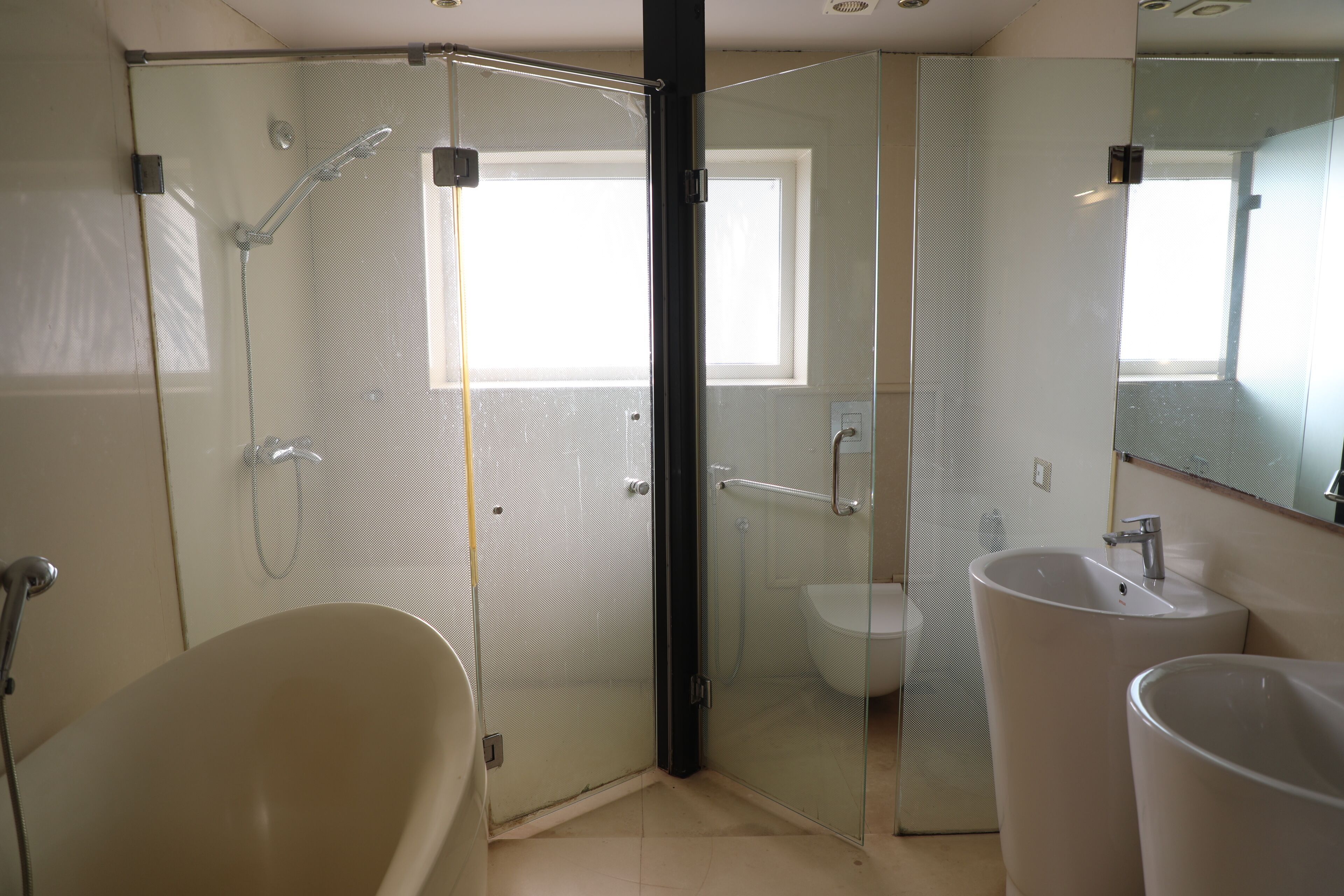 A modern bathroom with a glass-enclosed shower, a freestanding bathtub, and two sinks.