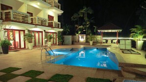 A swimming pool with a tiled deck, surrounded by potted plants and outdoor furniture. - White Pearl Suites by Rosetum (Calangute)