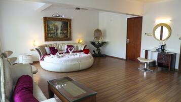A spacious living room with a round sofa, a coffee table, and a dining area with a chair and a small table.