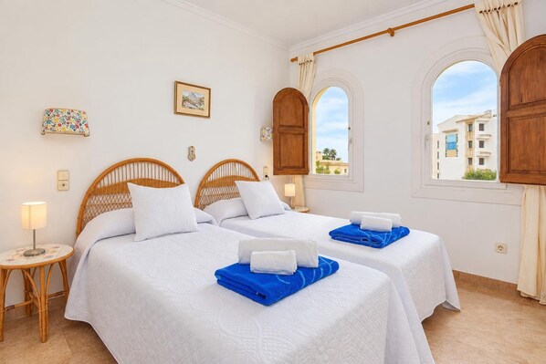 A hotel room with two beds, a small table, a lamp, and a window with a view of buildings. - Classic apartment  with communal pool in Javea, Costa Blanca, Spain for 4 persons (Javea)
