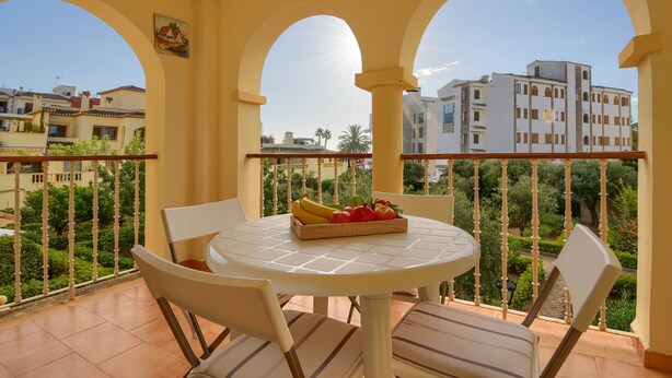 A balcony with a round table and chairs, a fruit basket, and a view of buildings and greenery. - Classic apartment  with communal pool in Javea, Costa Blanca, Spain for 4 persons (Javea)