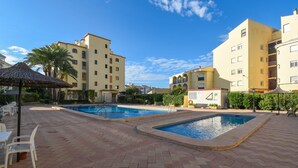 A swimming pool area with tiled flooring, a palm tree, and a building with balconies. - Classic apartment  with communal pool in Javea, Costa Blanca, Spain for 4 persons (Javea)
