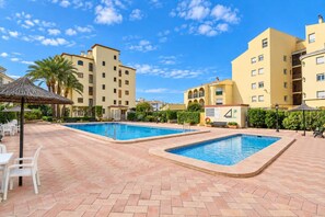 A hotel pool area with two swimming pools, lounge chairs, and palm trees. - Classic apartment  with communal pool in Javea, Costa Blanca, Spain for 4 persons (Javea)