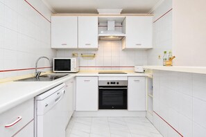 A compact kitchen with white cabinets, a microwave, a stove, and a dishwasher. - Classic apartment  with communal pool in Javea, Costa Blanca, Spain for 4 persons (Javea)