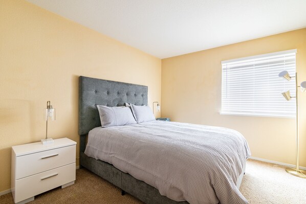 Une chambre à coucher avec un lit, une table de chevet, une lampe et une fenêtre avec des stores.