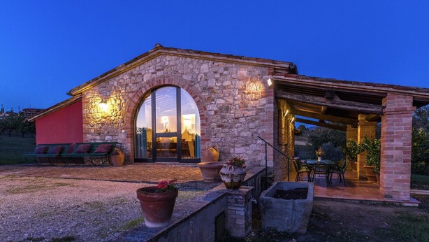 Un edificio in pietra con un'ampia porta ad arco, posti a sedere all'aperto e un patio con vasi di piante.
