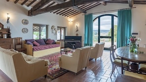 Relax in this inviting living room with a comfortable sofa set, dining table, and grand piano, offering a scenic view.