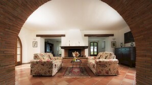 Un salon chaleureux avec deux fauteuils à motifs floraux, une table basse centrale et une cheminée.