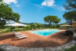 A rectangular swimming pool with a tiled deck, surrounded by lounge chairs and umbrellas, set against a backdrop of trees and hills. - Fonte Pinella 8 in Chiusi (Chiusi)