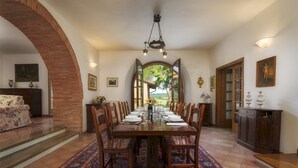 Un coin repas avec une longue table dressée pour le repas, entourée de chaises en bois. Une grande fenêtre offre une vue sur l’extérieur.