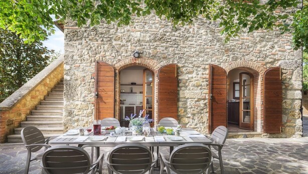 Un espace de restauration en plein air agrémenté d’un mur en pierre, de volets en bois et d’une table dressée pour quatre personnes.