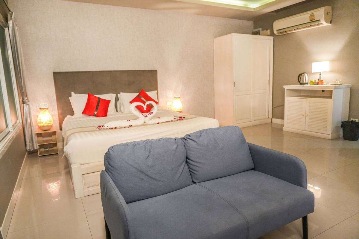 A hotel room with a bed, a blue armchair, a bedside table with a lamp, and a wardrobe.