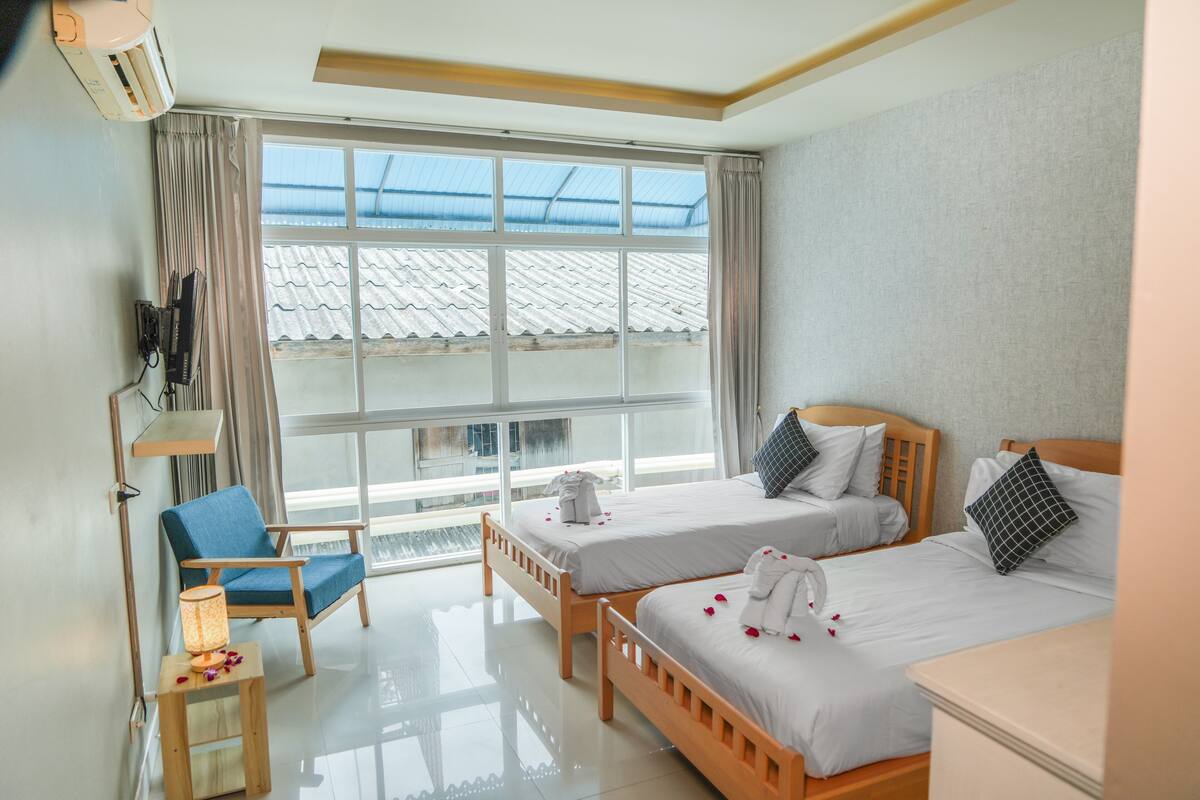 A hotel room with two beds, a chair, a small table, and a window with a view of a building.