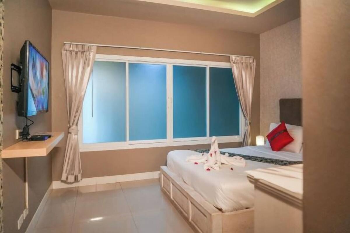 A hotel room with a bed, a TV, a window with curtains, and a bedside table.