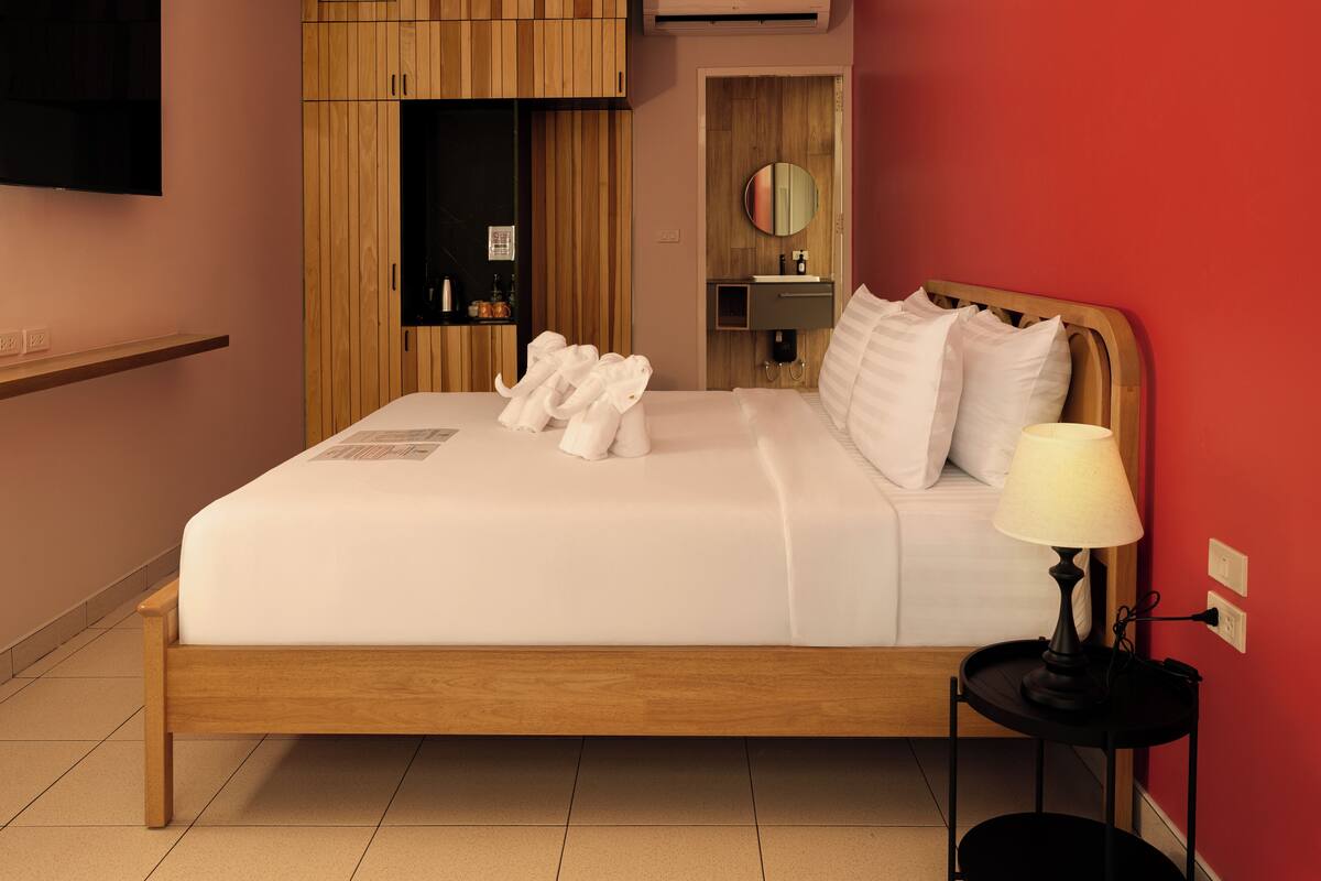 A neatly made bed with white linens and towels, a bedside lamp, and a wooden headboard.