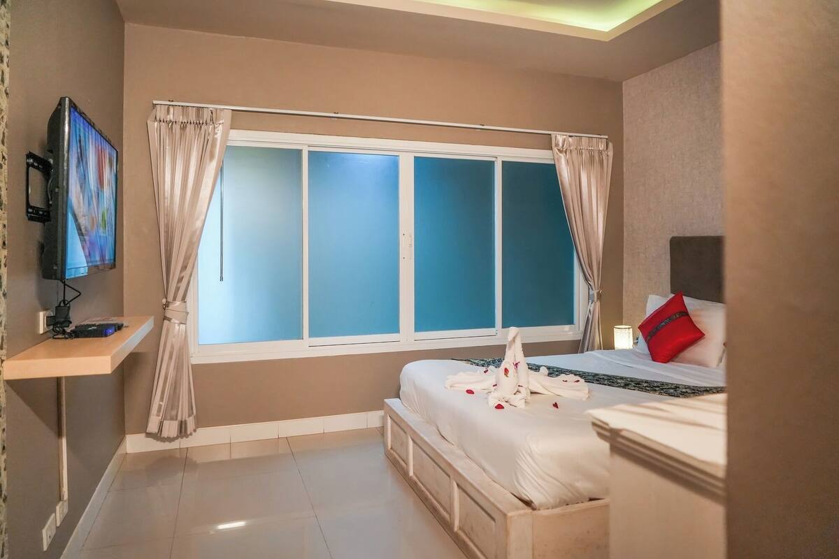 A hotel room with a bed, a TV, and a window with curtains.