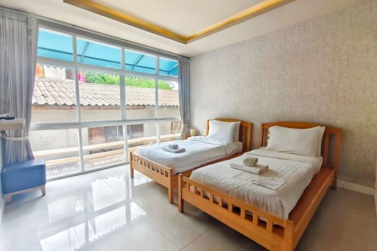 A room with two wooden beds, a large window with a view of buildings, and a blue chair.