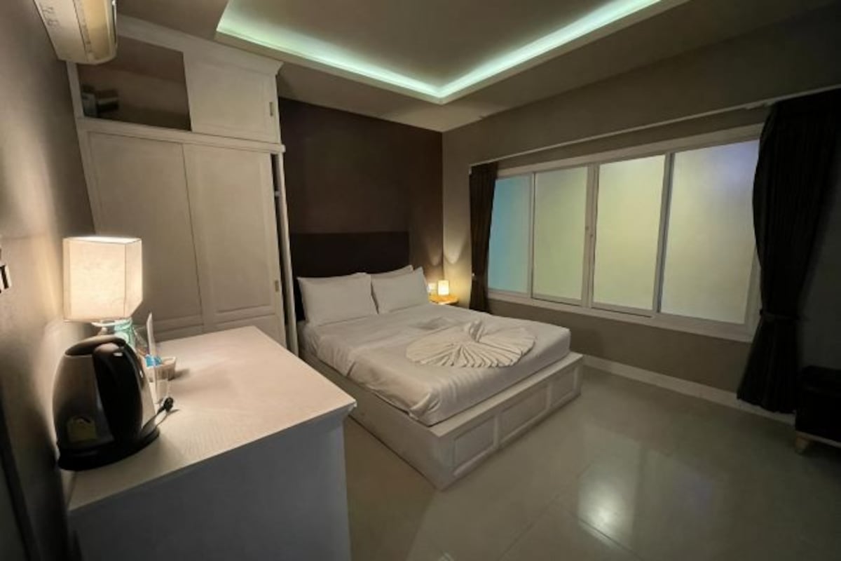 A hotel room with a bed, bedside table, lamp, and a window with curtains.