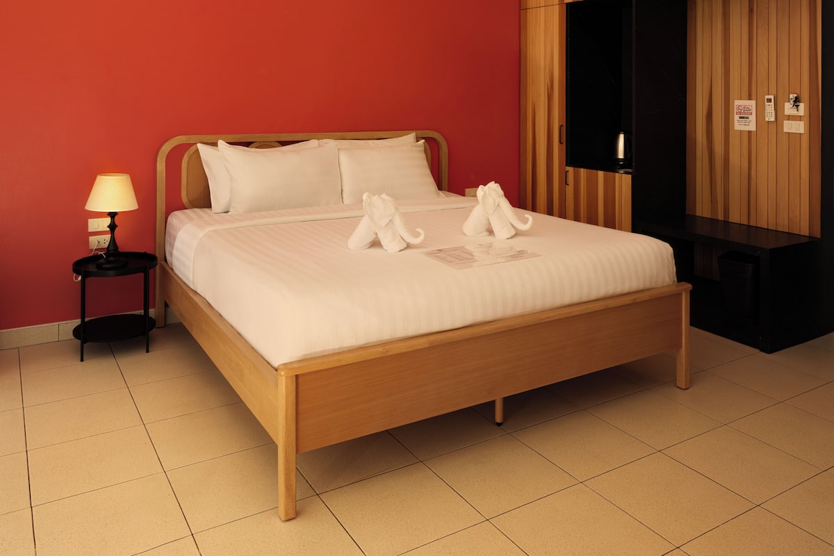A neatly made bed with white linens and two towels folded on top, a bedside lamp, a wooden nightstand, and a wardrobe with a mirror.