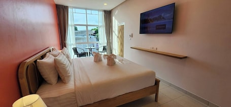 A hotel room with a large bed, a TV mounted on the wall, and a window with curtains.