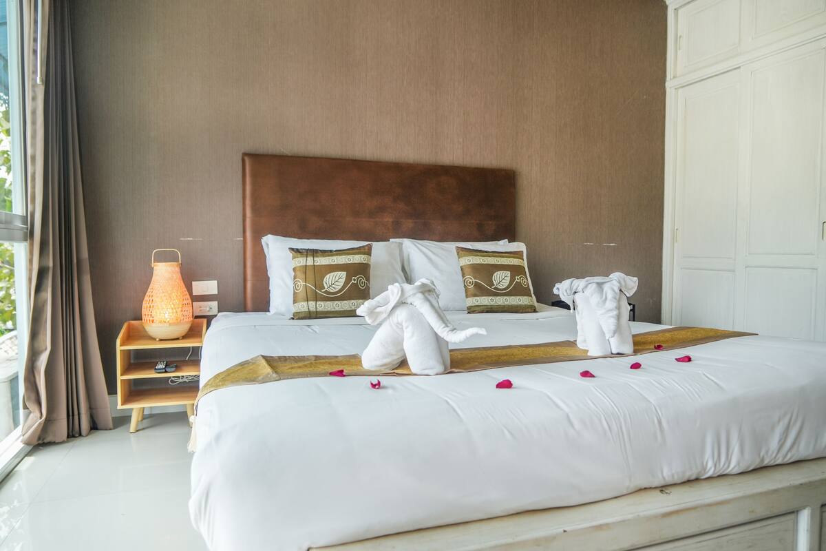 A neatly made bed with white linens and decorative pillows, a bedside lamp, and a wooden nightstand.