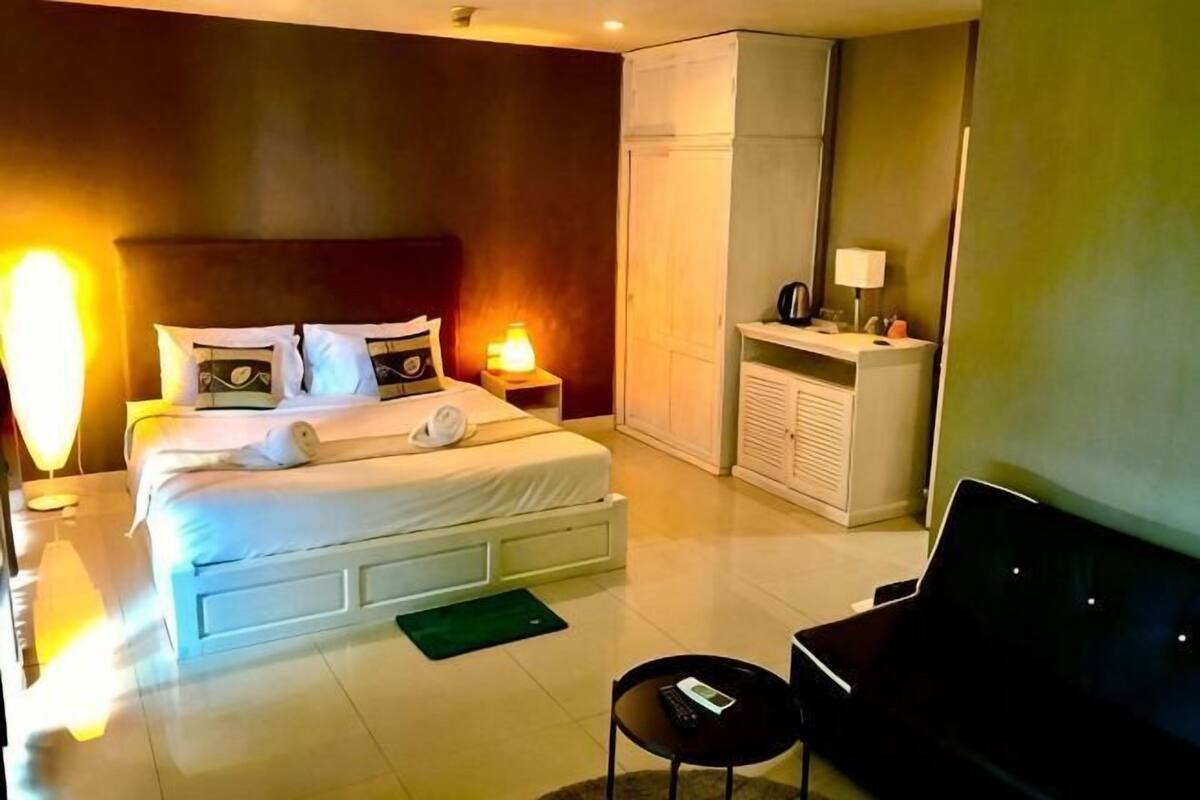A hotel room with a bed, bedside table, lamp, TV, and a small seating area.