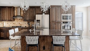 A modern kitchen with dark wood cabinets, stainless steel appliances, a marble island, and three bar stools. - Beautiful and Very Spacious house 6 bed/3.5 baths (Round Rock)
