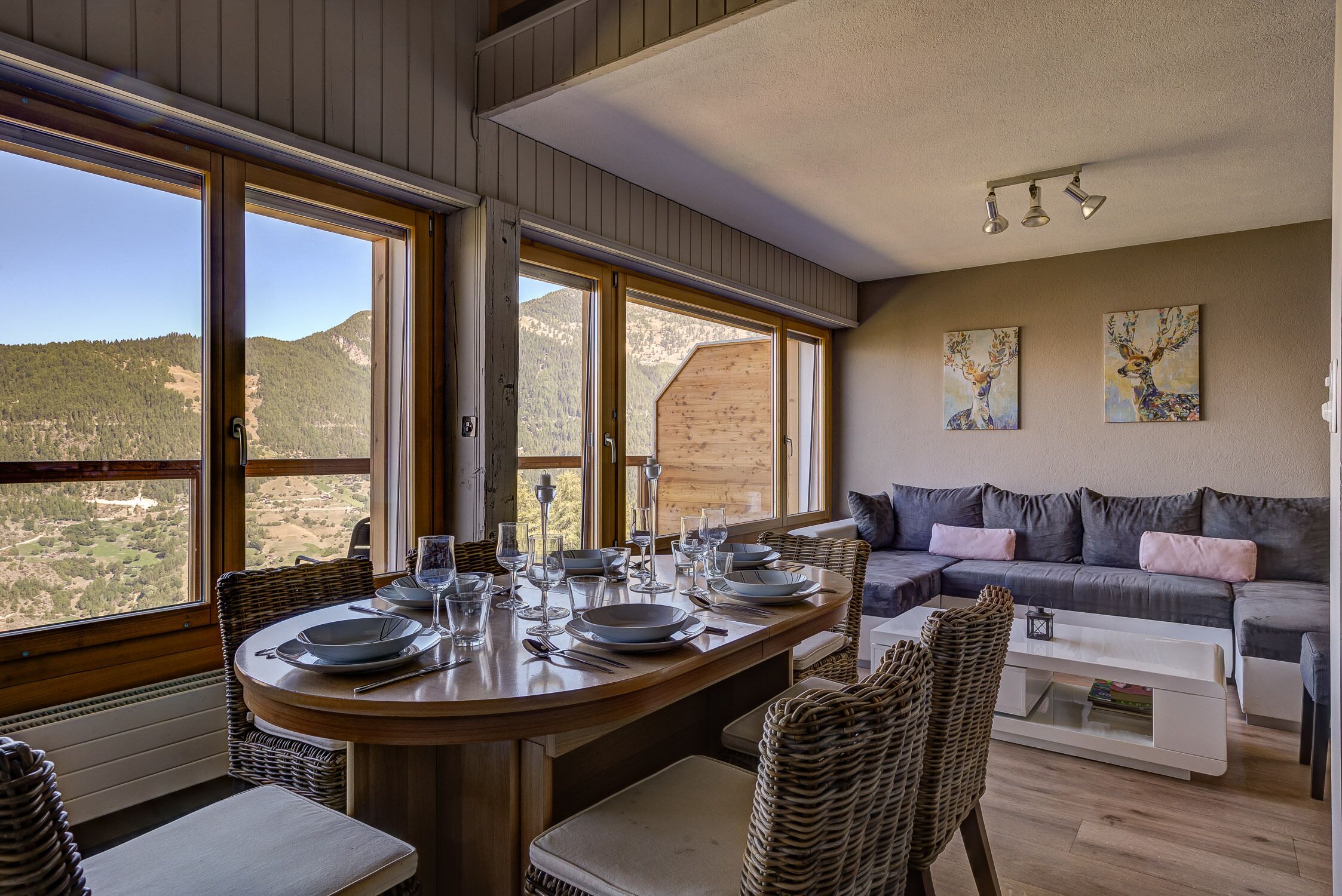 Un coin repas avec une table dressée pour quatre personnes, de grandes fenêtres, un canapé et des œuvres d’art accrochées au mur.