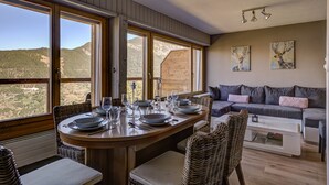 Un comedor con una mesa preparada para cuatro personas, ventanas grandes, un sofá y obras de arte en la pared.