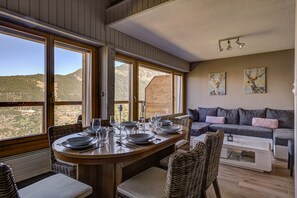 A dining area with a table set for four, large windows, a sofa, and artwork on the wall.