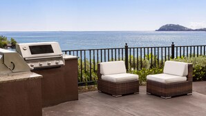 An outdoor patio with a grill, two wicker chairs, and a view of the sea. - Beachfront St Thomas Getaway - Family Friendly Resort Condo - Sleeps 8 (St. Thomas)