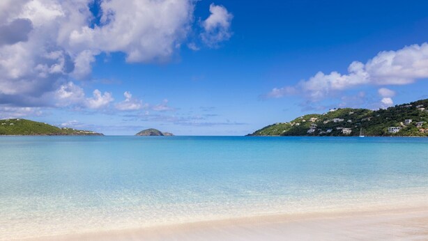A beach with clear turquoise water, a sandy shore, and a hilly landscape with buildings in the background. - Beachfront St Thomas Getaway - Family Friendly Resort Condo - Sleeps 8 (St. Thomas)