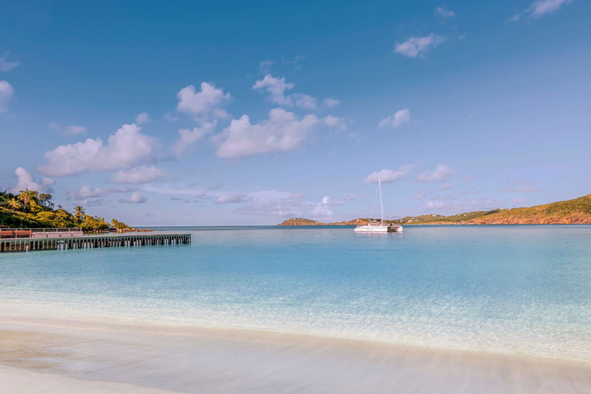 Una playa tranquila con un muelle que se adentra en el agua, un bote anclado cerca de la orilla y un cielo despejado.