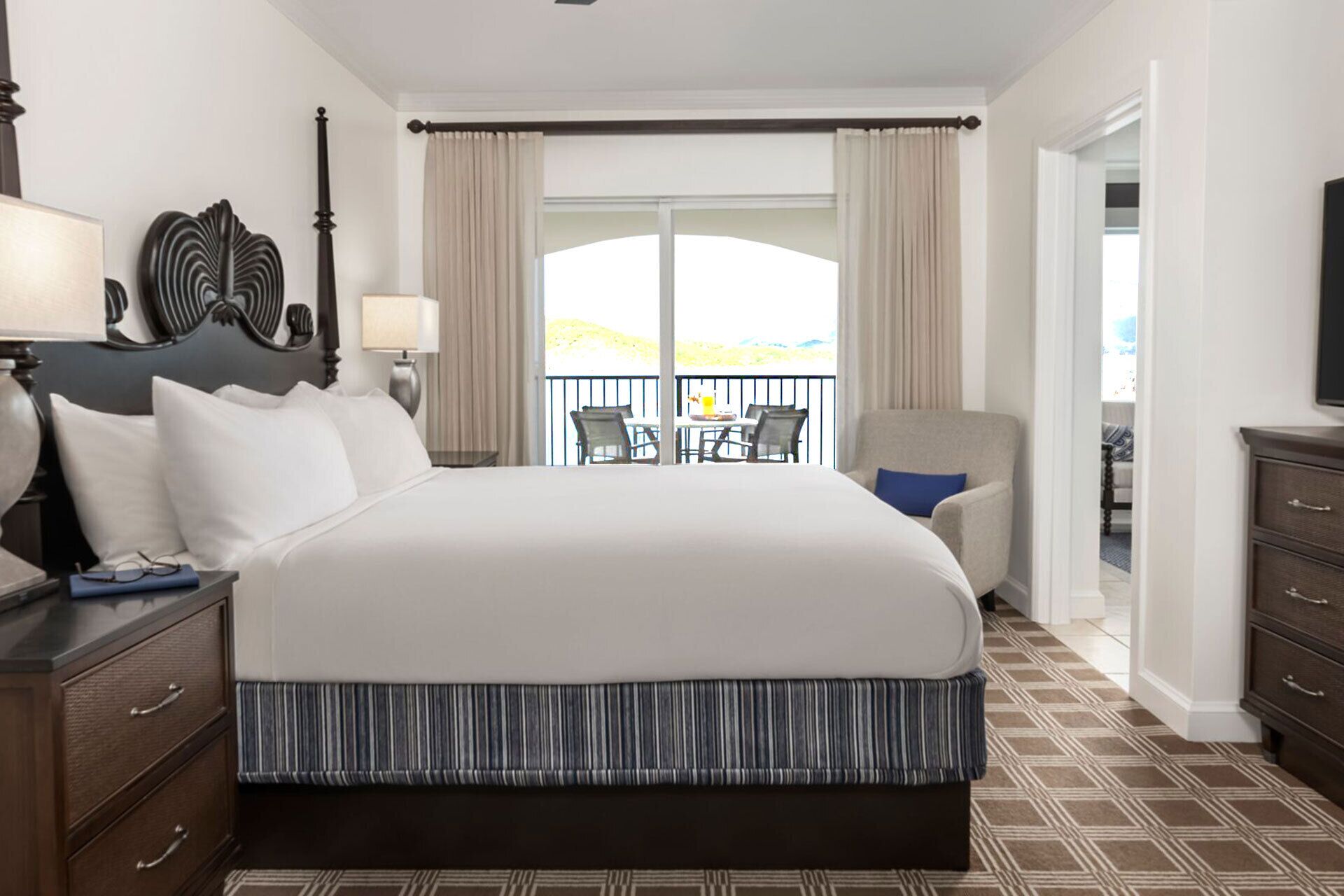 Habitación de hotel con una cama grande, una mesita de noche, un aparador y vistas al exterior.