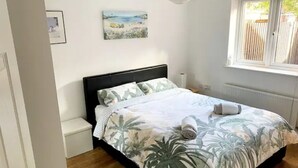 A bedroom with a bed, a nightstand, a window, and a painting on the wall.