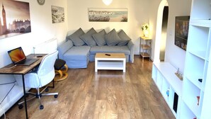 A modern living room with a sectional sofa, a wooden coffee table, a desk with a laptop, and a bookshelf.