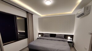 Un dormitorio moderno con una cama grande, mesitas de noche, un equipo de aire acondicionado y una ventana con cortinas.