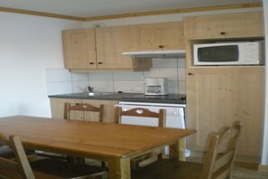 A small kitchen with wooden cabinets, a microwave, a coffee maker, and a table with chairs. - Cozy Chalet Stay w/ Pool (Notre Dame de Bellecombe)