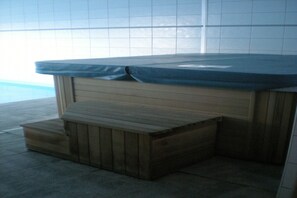 Un banc en bois recouvert d’une housse bleue, probablement placé près d’un jacuzzi, dans une pièce carrelée.