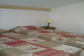 A single bed with a patterned bedspread, a bedside table with a lamp, and a wooden beam on the ceiling. - Cozy Chalet Stay w/ Pool (Notre Dame de Bellecombe)